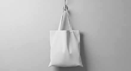 A plain white canvas tote bag hanging from a hook on a light gray wall, showcasing its simple design and material