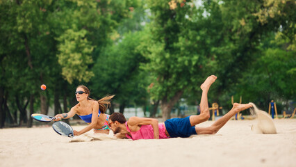Athletes falling in sand during intense beach padel rally. Concept of sports energy, psychology of...
