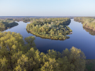 A river with a sharp turn and green trees. A picturesque bend in the river with an island covered in green trees, the leaves of which are just beginning to bloom