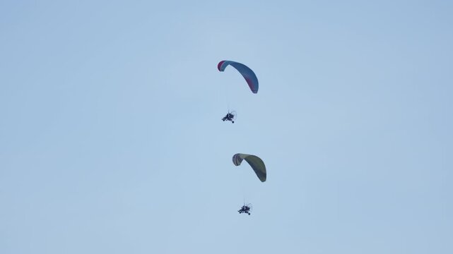 Technical visual depicts two operational paramotors, classified ultralight motorpowered paragliders, performing controlled flight maneuvers against completely unblemished, light blue sky under bright