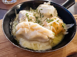 Assorted dumplings with cheese and chives in a skillet on wooden board
