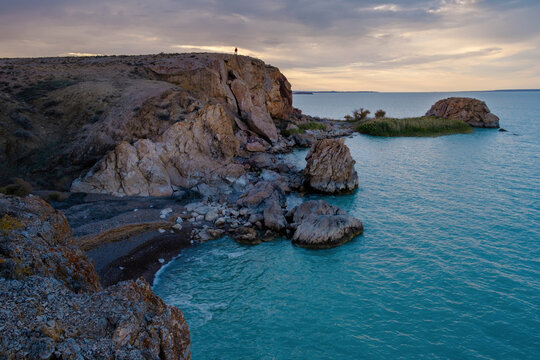 Rocky and beautiful shore of Lake Balkhash in Kazakhstan with turquoise water on an autumn day with a man on the rocks.