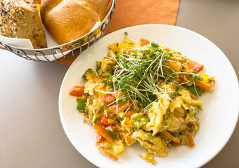 Colorful vegetable scrambled eggs with fresh bread and microgreens on a white plate