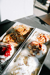 Delicious cinnamon rolls topped with cream and fruit at a sunny café table