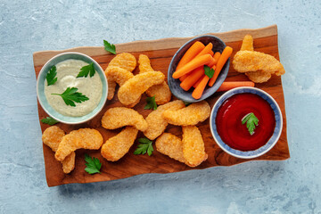 Chicken nuggets with fresh vegetables and dips, on a wooden board, overhead flat lay shot