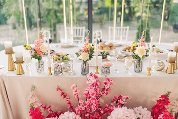 Elegant dining setup features fresh flowers, candles, and delicious food in a bright venue surrounded by nature