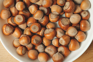 Assorted hazelnuts displayed in a white bowl on a wooden surface
