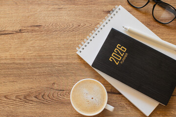 Stylish Desk Setup With 2026 Planner, Notebook, Pencil, Glasses, and Coffee on Wooden Surface