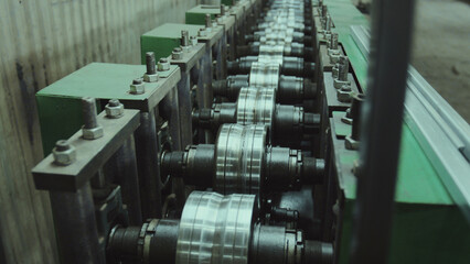 Obraz premium Industrial equipment with a series of mechanical rollers shaping long metal sheets into specific profiles, showcasing the manufacturing process in a steel processing factory