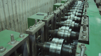Obraz premium Industrial machine processing sheet metal using a series of precisely aligned steel rollers, showcasing the automation and technology involved in modern factory production lines
