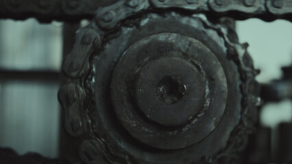Greasy metal industrial chain working on a gear, showing detail of mechanical parts engaged in motion, representing concepts of industry, strength, and continuous manufacturing
