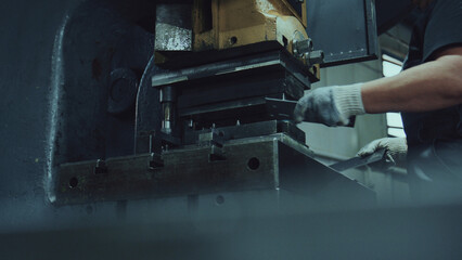 Worker hands, clad in protective gloves, operating a heavy industrial press machine, carefully guiding a metal sheet for precise stamping in a manufacturing factory environment