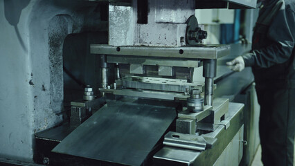 Heavy industrial metal press machine processing raw metal sheets, punching and forming components with precision in a modern manufacturing workshop, featuring a worker engaged in production