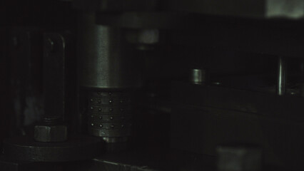Dark view of a heavy industrial machine featuring various metallic mechanical components, including a textured cylinder and securing bolts, conveying a sense of manufacturing and internal workings