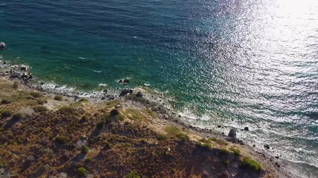 Aerial footage capturing the coastal scenery on the way to the ancient city of Knidos in Turkey. The video showcases the shimmering turquoise waters of the Aegean Sea meeting a rugged, sun drenched co