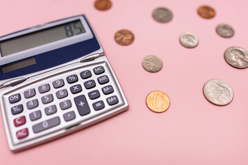 close-up of a compact calculator and scattered change including dimes, pennies, and nickels against a pink background in a horizontal orientation