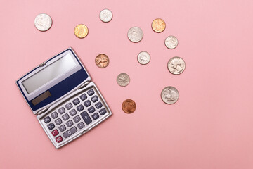 flat lay of a compact calculator and scattered change including dimes, pennies, quarters, and nickels against a pink background in a horizontal orientation