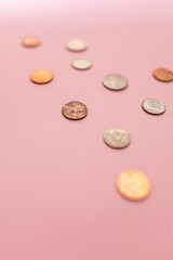 close-up of change including pennies, nickels, and dimes against a pink background blurred in a vertical orientation 