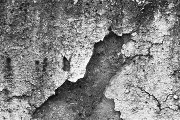 Black and white abstract background of rough, weathered concrete wall with large crack. This aged, grunge texture shows decay and damage on old plaster surface