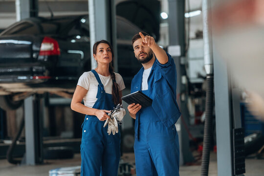 Digital tablet is in hands. Auto repair shop employees are working together. Man and woman