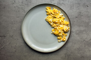 freshly scrambled eggs on a gray plate centered on a gray textured background