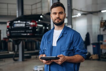 Modern digital tablet is in hands. Male mechanic is working in the car workshop