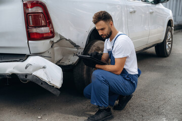 Rear part is in bad condition. Mechanic is sitting by the damaged pickup truck outdoors © standret