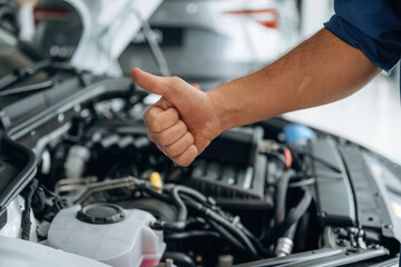 Done, showing thumb up, hood is opened. Close up view of male service station worker at job