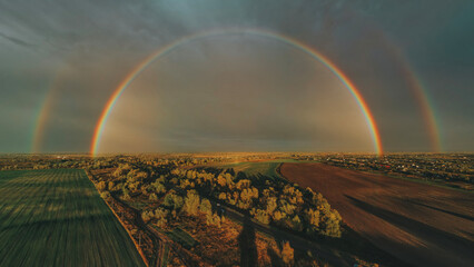defaultAn aerial shot of a vibrant, full rainbow over an autumn landscape. The vibrant, saturated colors of the rainbow contrast with the overcast sky and earthy tones of the fields.