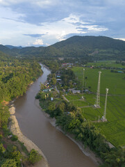 Fototapeta premium Aerial river valley landscape. Lush green forest meets rural fields and mountains. Communication tower infrastructure stands, blending nature with progress, creating peaceful, reflective mood