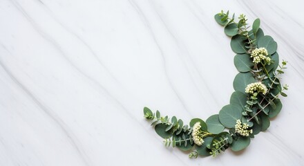 A crescent-shaped arrangement of green eucalyptus leaves and small white flowers rests on a white marble surface with light grey veining