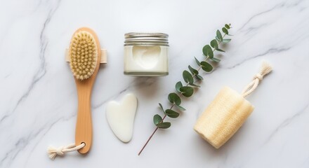 A dry brush cream jar gua sha tool eucalyptus sprig and loofah sponge are arranged on a white marble surface