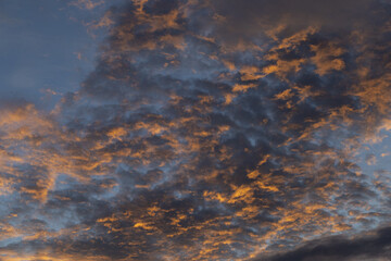 Dramatic sky patterns feature scattered cloud formations bathed golden, orange, and blue light. atmospheric display captures essence of serene sunset or vibrant sunrise, offering peaceful natural
