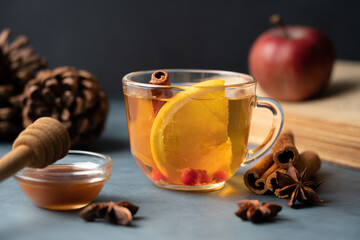 Glass cup of orange tea with cinnamon on a dark background, cozy aromatic hot drink for autumn and winter season