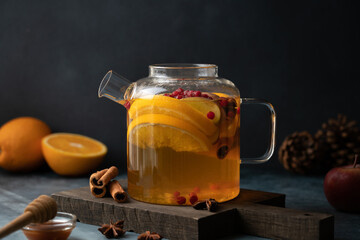 Side view of teapot with orange and apple tea infused with cinnamon on a dark background, cozy autumn and winter beverage concept