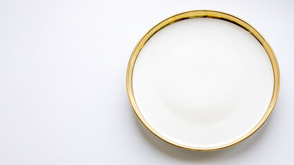 Simple white plate with gold rim placed on a light surface suitable for background.