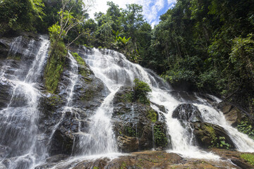 Fototapeta premium Majestic waterfall cascade tumbles with pure water over mossy rock in vibrant tropical jungle forest. This lush green environment offers powerful, serene, and beautiful natural flow