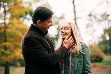 Fototapeta premium Senior couple sharing a tender moment, man's hand caressing woman's face, in an autumn park