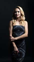 Blonde woman posing confidently in a stylish black strapless paisley dress on a dark background
