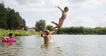 Family on vacation splashing in a lake. Kid girl jumping in outdoor in a lake. Happy grandparents with grandchild enjoying summer vacationthe and plays in the river. 