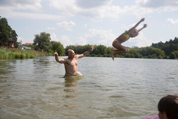 Family on vacation splashing in a lake. Kid girl jumping in outdoor in a lake. Happy grandparents with grandchild enjoying summer vacationthe and plays in the river. 
