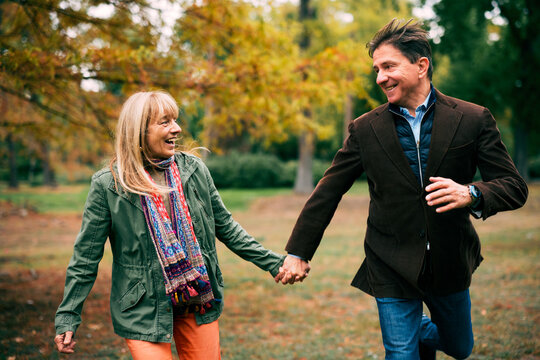 Fototapeta Happy mature couple holding hands running in autumn park