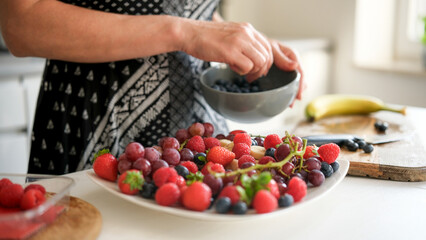 Woman Putting Grapes, Strawberries, Raspberries, Blueberries, And Bananas On A Plate