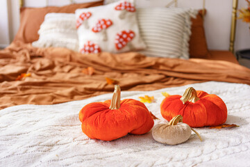 Soft decorative pumpkin pillows on cozy bed with warm autumn colors, creating a seasonal fall atmosphere. Decorative plush cushions on blanket in bedroom interior, home decor