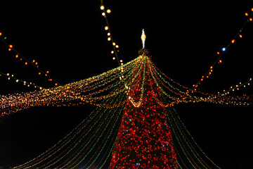 Brightly illuminated big Christmas tree decorated with garlands with shinig lights and ornaments at night, creating festive holiday atmosphere. Christmas and New Year holiday fair outdoor.