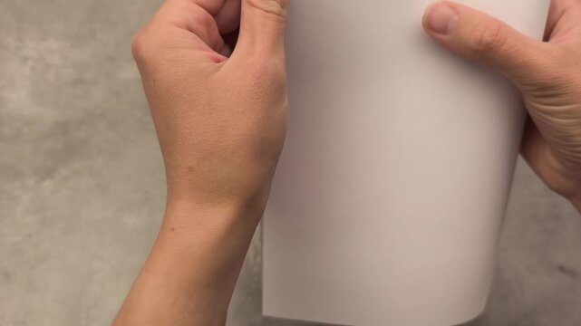 Hands are preparing a blank sheet of paper on a textured surface, demonstrating the initial steps of a creative project with focused attention and intention