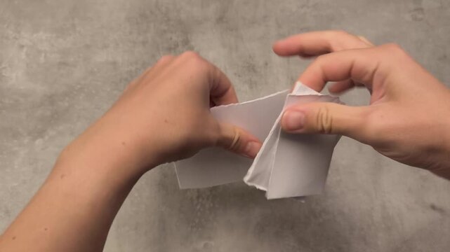 Hands demonstrate the process of tearing paper in a sequential motion, showcasing the gradual progression of the action and texture of the material