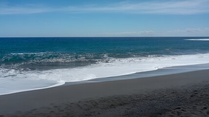 Black sand beach with gentle ocean waves and blue sky.