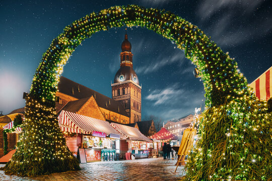 Riga, Latvia. Traditional Christmas Market On Dome Square With Cathedral. Famous Landmark In Winter Evening Night In Festive Illuminations Lighting