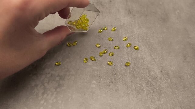 Hand pouring yellow beads from a clear container onto a textured surface, capturing the dynamic flow of the beads in a continuous motion sequence